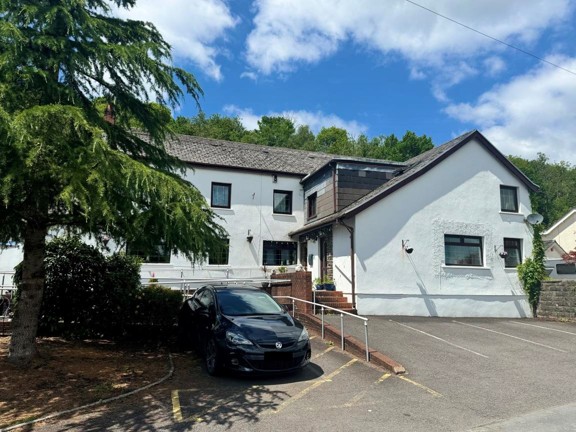 Exterior of Ty Camlas, a white-rendered care home with a slate roof, parking area and wooded hillside behind