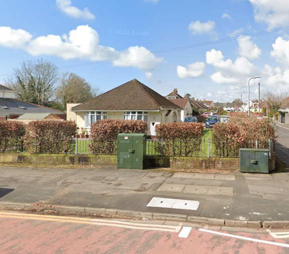 Street view of Dyfan Court, a single-storey bungalow with a hipped roof behind a hedge and railings