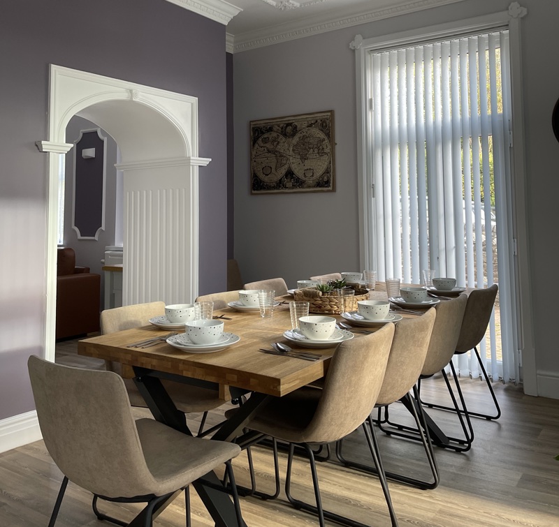Dining area at Brynawel with a set wooden table, beige chairs and an arched opening to the lounge