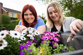 Two people tending pink and white flowers in a garden planter outside Cae Deri