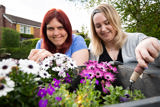 Two people tending pink and white flowers in a garden planter outside Cae Deri