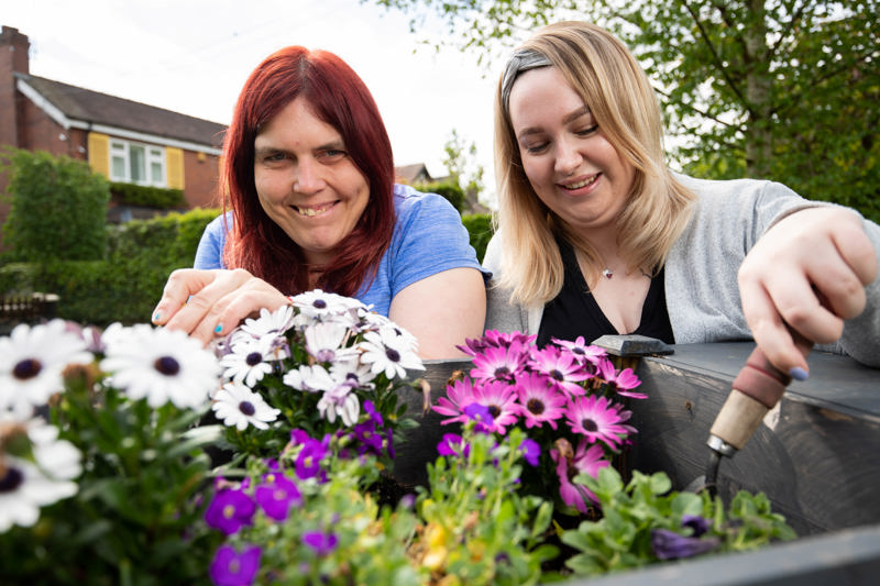 Two people tending pink and white flowers in a garden planter outside Cae Deri