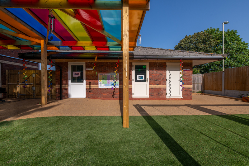 Garden playground with bright green grass and a undercover area with rainbow glass roof.