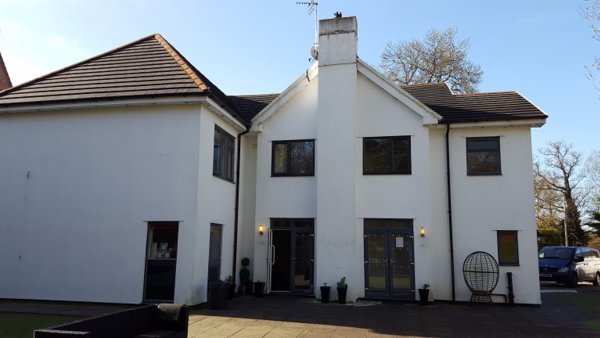 White-rendered two-storey exterior of The White House with dark-framed windows, a central chimney and a paved patio