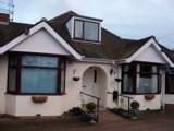 White-rendered front exterior of Maycroft, a bungalow with bay windows, a dormer and hanging baskets