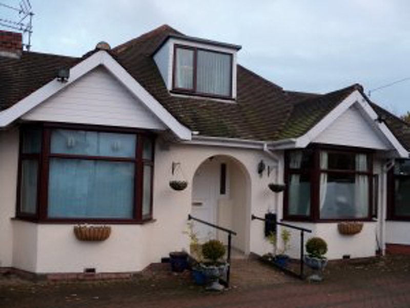 White-rendered front exterior of Maycroft, a bungalow with bay windows, a dormer and hanging baskets