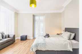 Spacious bedroom at Brynawel with a grey upholstered bed, a sofa and French doors to a balcony