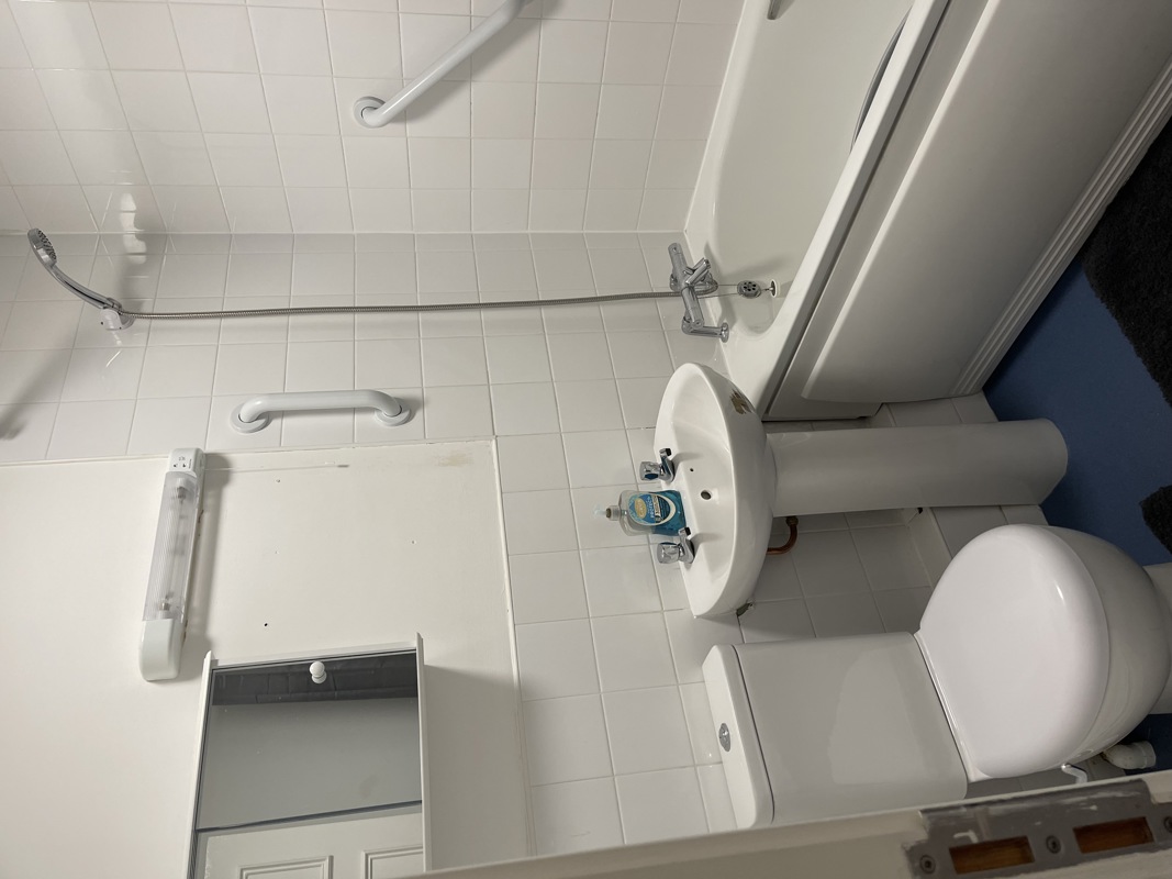 Accessible bathroom at Glanmore with a toilet, basin, grab rails and white tiled walls