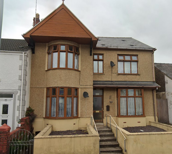 Front exterior of Ffordd Newydd, a pebbledashed house with bay windows, a timber gable and steps to the front door