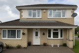 Front exterior of Cae Eithin, a yellow-brick detached house with a white front door, bay windows and a paved drive