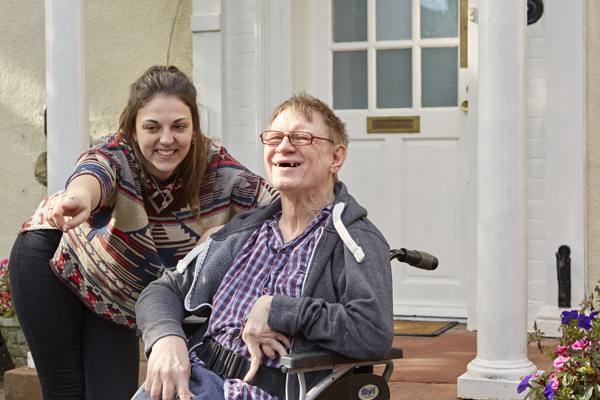 A support worker and a resident smiling together at the front door of Blackwells