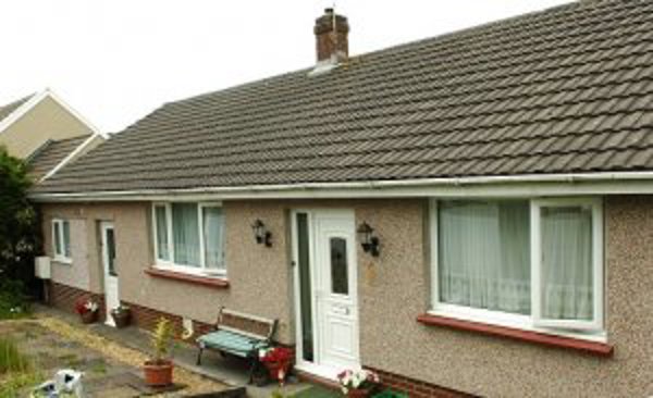 Front exterior of Howells Road, a pebble-dashed bungalow with a white front door and a garden bench