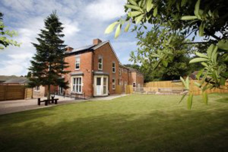 Exterior of The Chantry, a red-brick house with white-framed windows, a large lawn and a fenced garden