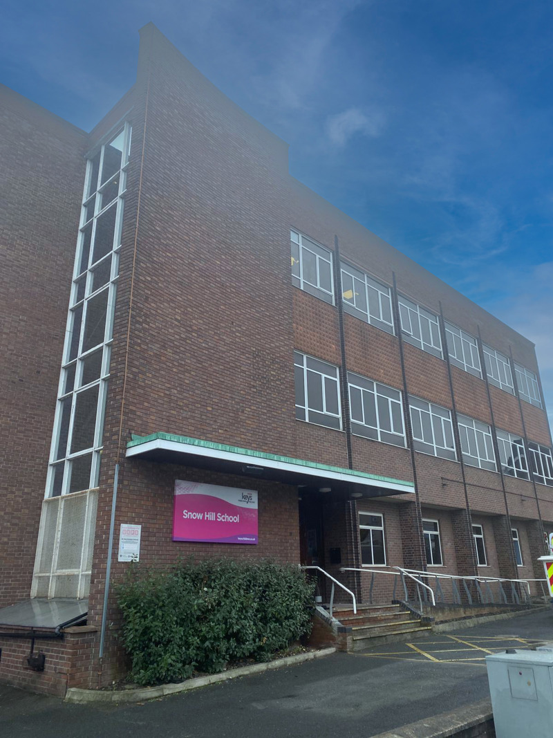 Brown-brick three-storey exterior and entrance of Snow Hill School with a pink sign and a tall glazed stairwell