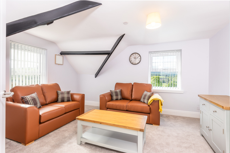 Loft lounge at Brynawel with tan leather sofas, exposed black beams and a window with countryside views
