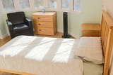 Bedroom at Evergreen with a bed, oak chest of drawers and an armchair in a sunny bay window