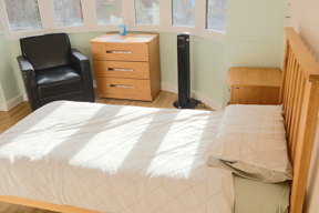 Bedroom at Evergreen with a bed, oak chest of drawers and an armchair in a sunny bay window