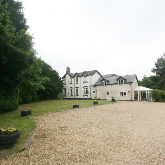 Front exterior of Maple Leaf Lodge, a white house with a gravel drive, lawn and conservatory