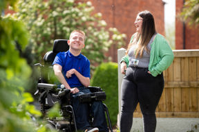 A man in a powered wheelchair chatting with a support worker in the garden beside the building at The Haven