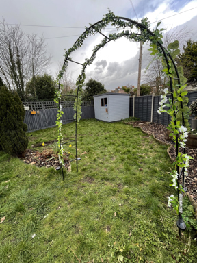 Lawned garden with archway trellis and grey garden shed with grey fencing.