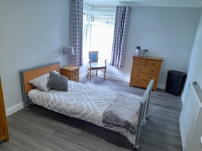 Single bedroom at Boston House with a profiling bed, grey patterned bedding and a bay window