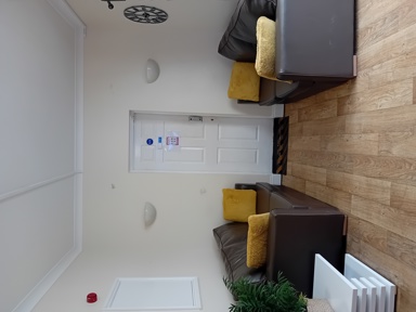 Communal lounge at Eynesbury House with brown leather sofas, mustard cushions and wood-effect flooring