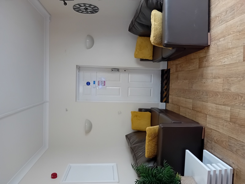Communal lounge at Eynesbury House with brown leather sofas, mustard cushions and wood-effect flooring