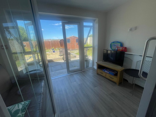Lounge at Rosewood with patio doors onto the garden, a TV on a wooden stand and children's toys