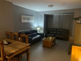 Living room at Byron Lodge with black leather sofas and a wooden dining set